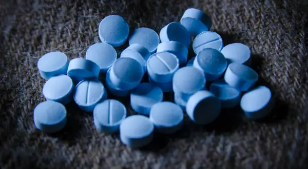 En hög med blå tabletter, som kan associeras med bensodiazepiner biverkningar, ligger på en grov, brun yta.