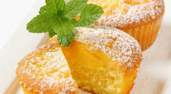 Två fluffiga citronmuffins, pudrade med florsocker och garnerade med mynta. Perfekt för ett enkelt citronmuffins recept.
