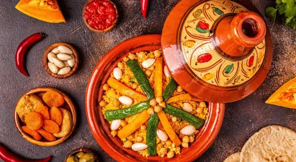 Un colorato cous cous marocco, con verdure, mandorle e albicocche secche, servito in una tajine decorata.