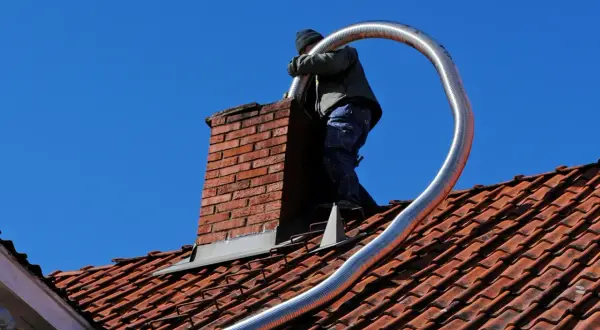 Un couvreur effectue l'installation tubage cheminée sur un toit en tuiles rouges, sous un ciel bleu éclatant.