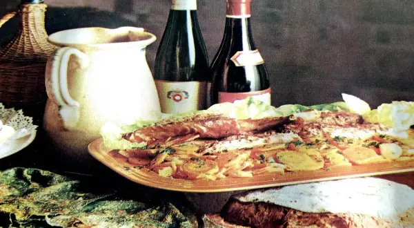 Un banchetto con pesce, verdure e pane fresco, accompagnato da vino e brocca. Sapori autentici del **chilometro zero Rodi Garganico**.