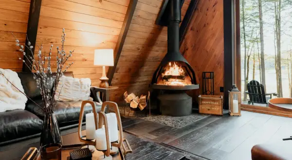 Salon cosy avec cheminée ventouse crépitante, canapé en cuir et vue sur la forêt.