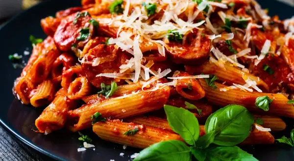 Penne z krewetkami w sosie pomidorowym, posypane parmezanem i udekorowane bazylią.