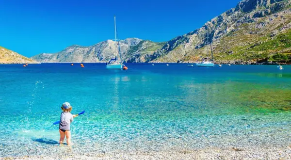 Dziecko bawi się na kamienistej plaży w Grecji. Marzysz o tanich lotach z Krakowa gdziekolwiek? To miejsce czeka!
