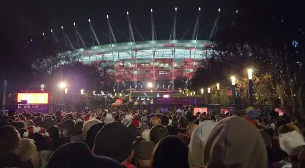 Tłum ludzi zmierza na roztanczony PGE Narodowy. Stadion oświetlony na czerwono, nocna atmosfera.