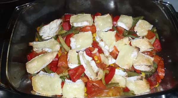 Zapiekanka z warzywami i kawałkami sera camembert w szklanym naczyniu.
