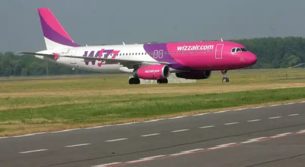 Samolot Wizz Air z różowym kadłubem i fioletowym ogonem na pasie startowym.