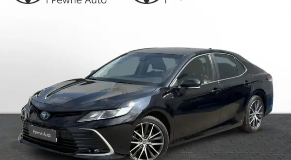 Elegancka, czarna Toyota Camry z napisem "Pewne Auto" na grillu. Lśniący lakier odbija światło, podkreślając dynamiczną sylwetkę sedana.