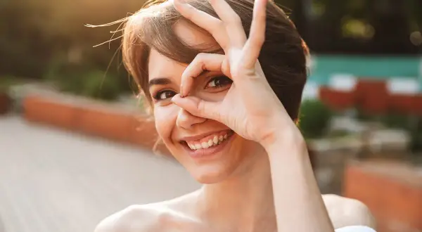 Uśmiechnięta kobieta z ręką przy oku, jakby szukała czegoś. To świetne mentalizacja przykłady, jak patrzeć na świat z ciekawością.