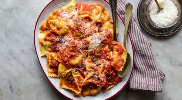 Piatto di tortelli di patate fatti in casa, conditi con sugo rosso e parmigiano grattugiato, pronti per essere gustati.