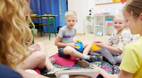 Dzieci siedzą na podłodze, bawiąc się zabawkami. To świetny sposób, jak uczyć dzieci angielskiego przez zabawę.
