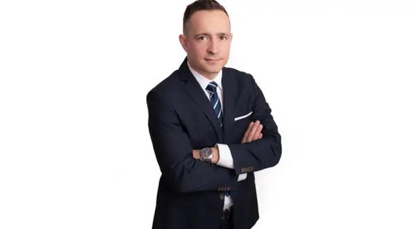 Mężczyzna w garniturze ze skrzyżowanymi rękami, na białym tle.