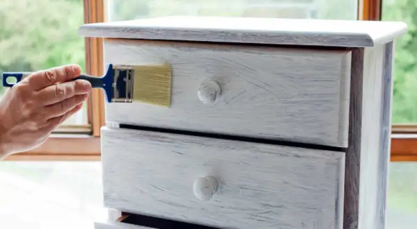 Restauro di un comò con chalk paint: un pennello applica la vernice per un look shabby chic.