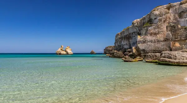 Acque cristalline e scogliere imponenti definiscono la spiaggia più bella del Salento. Faraglioni emergono dal mare turchese, un vero paradiso.
