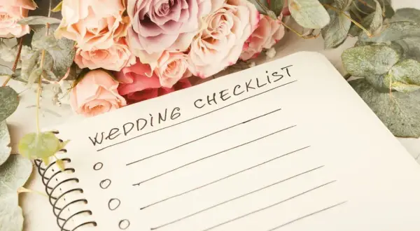 Bukiet róż i eukaliptusa obok notatnika z napisem "Wedding Checklist". Planowanie wesela w lesie zaczyna się od listy zadań.