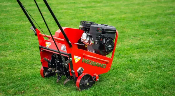 Czerwony aerator WEIBANG na zielonym trawniku, gotowy do pracy. To urządzenie zapewnia doskonałą aerację trawnika, poprawiając jego wygląd i zdrowie.
