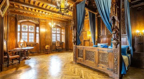 Luksusowe noclegi zamek Czocha: bogato zdobiona sypialnia z baldachimem, witrażami i drewnianymi panelami.