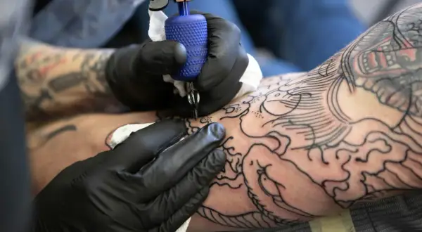 Artysta w czarnych rękawiczkach tworzy na ramieniu skomplikowany wzór irezumi, dodając kolejne linie do smoka i fal.