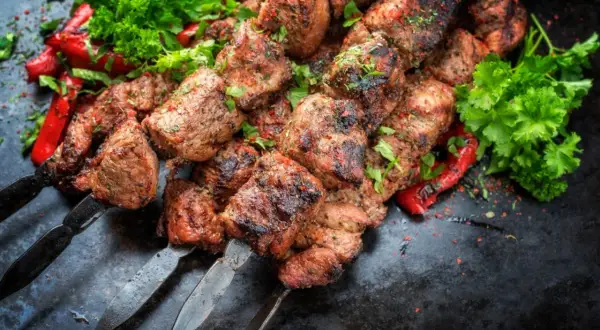 Soczysty kebab gruziński na metalowych szpikulcach, ozdobiony świeżą natką pietruszki i papryką.