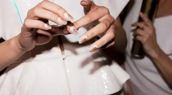 Mani con unghie bianche e dettagli dorati. Chissà quanto ci mette lo smalto ad asciugare per un look così perfetto.