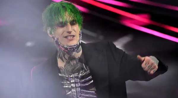 Theo la sad, con capelli verdi e trucco drammatico, indossa un abito nero e una maschera metallica.