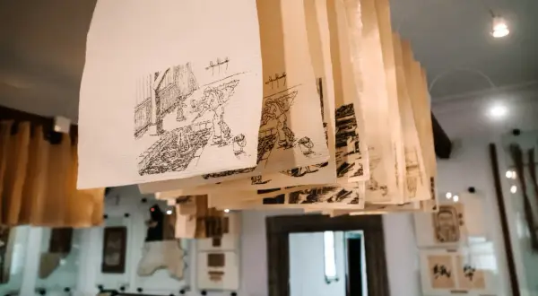 Rzędy ręcznie rysowanych scen na papierze czerpanym wiszą pod sufitem, tworząc unikalną galerię.