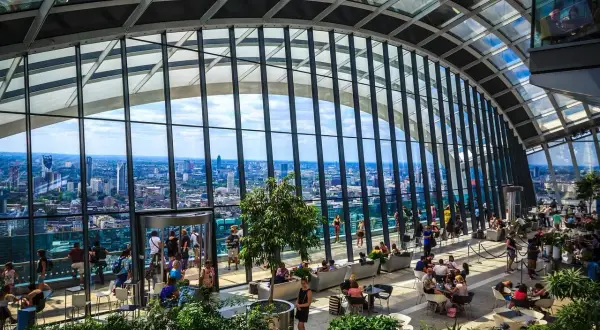Relaks w Sky Garden w Londynie. Ludzie odpoczywają wśród zieleni, podziwiając panoramę miasta przez szklany dach.