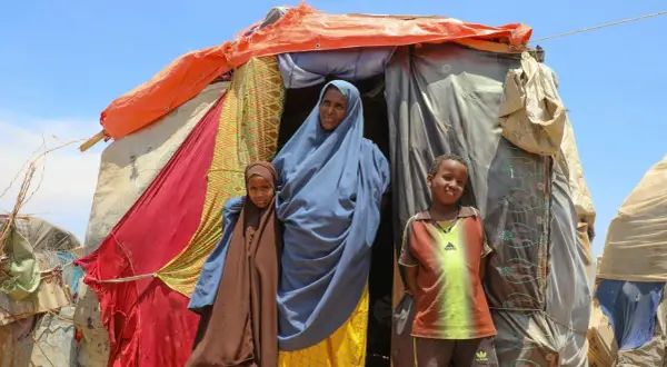 En kvinna och två barn står framför ett provisoriskt boende i Somalia. Deras historia är en del av Somalias historia.