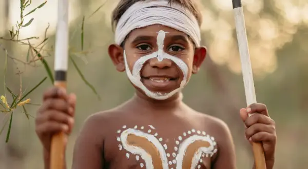 Giovane membro del popolo australiano con pittura facciale e corporea tradizionale, impugna lance.