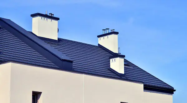 Nowy dom z ciemnym, łupkowym dachem bezokapowym i białymi kominami, pod błękitnym niebem.
