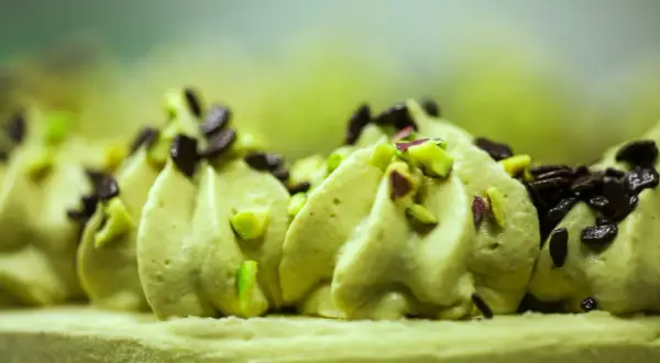 Delikatna beza z kremem pistacjowym, ozdobiona posiekanymi pistacjami i czekoladą.