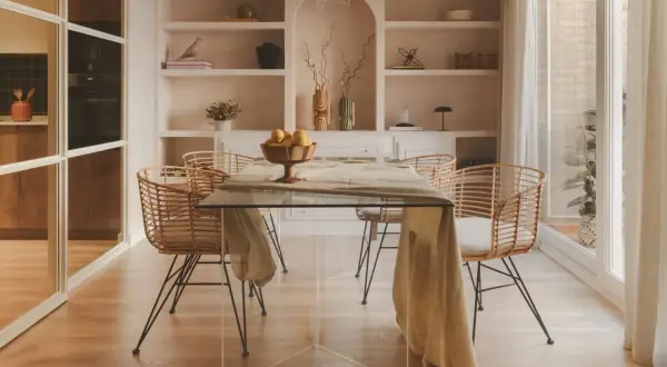 Comedor moderno con mesa de cristal y sillas de ratán. Estanterías empotradas con decoración. El precio del proyecto de interiorismo se ajusta a este estilo.