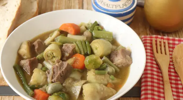 Un reconfortante plato de menestra de ternera con trozos de carne tierna y verduras como alcachofas, judías verdes y zanahorias.