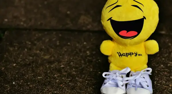 Żółta maskotka z napisem "Happy..." i śmiesznymi cytatami na twarzy, w białych trampkach.