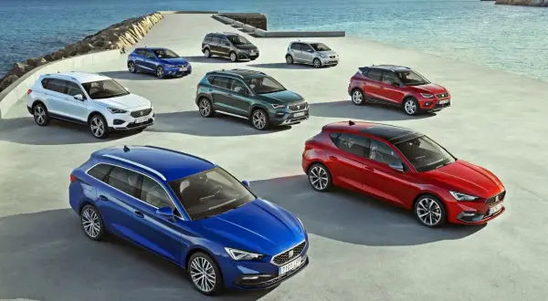 Różnorodne modele SEAT stojące nad morzem. Kolekcja aut SEAT, od kompaktowych po SUV-y, prezentuje się na tle błękitnego oceanu.