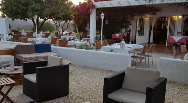 Mesas puestas en el exterior de un restaurante con un bar aguamarga. Ambiente tranquilo bajo la luz del atardecer.