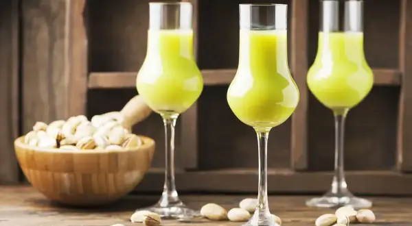 Zielony likier pistacjowy w kieliszkach, obok miseczki z pistacjami. Idealny przepis, jak zrobić wódkę ze spirytusu, by uzyskać taki smak.