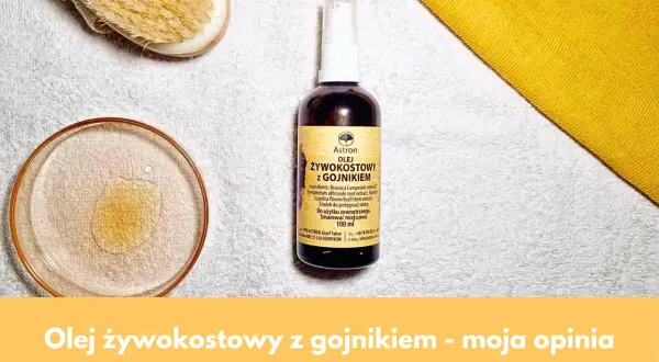 Olej żywokostowy z gojnikiem w buteleczce z atomizerem, obok kieliszka z płynem i szczotki do masażu. Naturalna pielęgnacja.