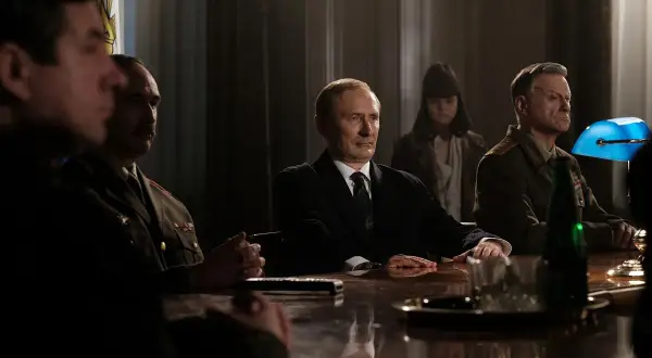 W nowym filmie Vegi, mężczyźni w mundurach i garniturze siedzą przy stole.