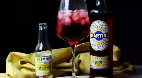 Czerwony drink z lodem, obok butelka Martini Vibrante i Artonic Indian Tonic Water. Idealny na letnie popołudnie.
