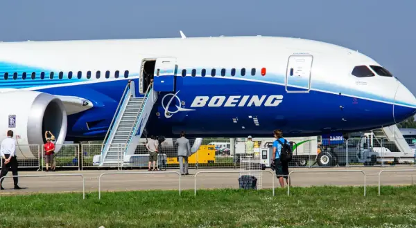 Ogromny samolot Dreamliner Boeing z otwartymi drzwiami i schodkami. W tle ludzie i sprzęt lotniskowy.