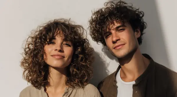Ein junges Paar mit vollen Locken vor einer weißen Wand. Die curly girl lächelt sanft.