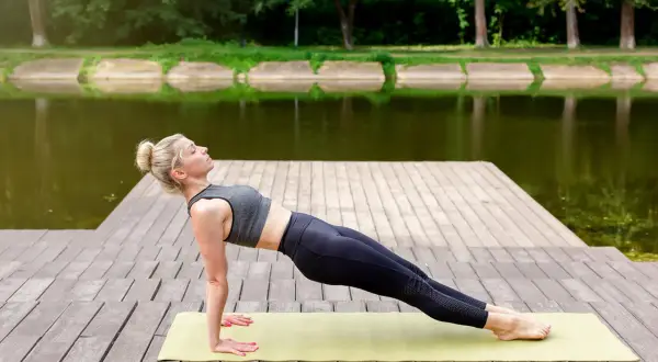 Kobieta wykonuje ćwiczenie reverse plank na macie na drewnianym pomoście nad jeziorem.