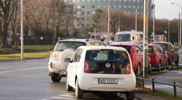 Biały Volkswagen up! i inne samochody stojące na jezdni, częściowo zasłaniające przejście dla pieszych.