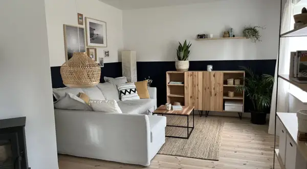 Salon moderne avec canapé gris, meuble en bois et tapis en jute. Le mur est peint en deux tons, blanc et bleu nuit, rappelant des techniques de peinture acrylique.
