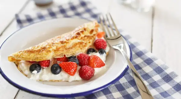 Słodki omlet z serkiem i owocami leśnymi, posypany cukrem pudrem. Idealny na pyszne śniadanie.