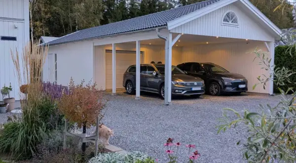 Vitt garage med två bilar under taket. En katt smyger i rabatten framför. Perfekt för att bygga garageport.