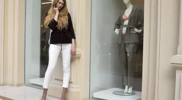 Modelka w białych spodniach i bordowym żakiecie obok manekina w szarym komplecie. Inspiracja skandynawskie marki odzieżowe.