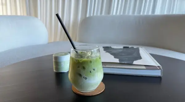 Un verre de tisane matcha glacée, avec une paille noire, à côté d'une boîte de matcha et d'un livre.