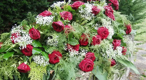 Bogactwo czerwonych róż i drobnych białych kwiatów tworzy elegancki wieniec pogrzebowy, symbolizujący pamięć i szacunek.